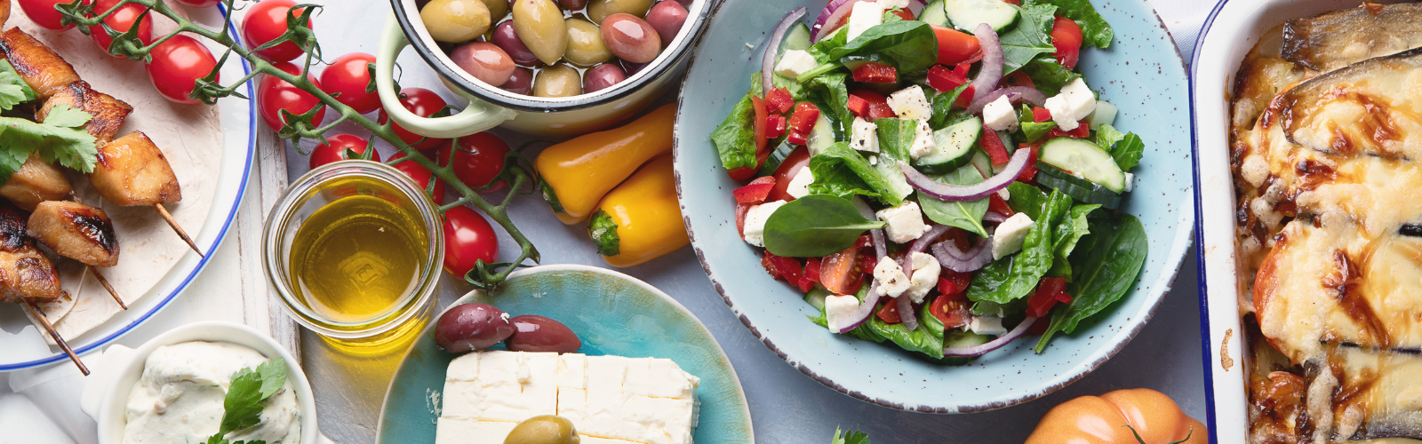 Table of traditional Greek dishes, including: feta cheese, olives, kebabs, and Greek salad.